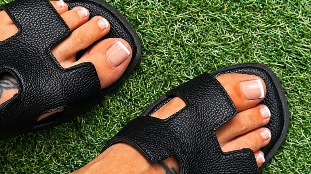 Verzorgde voeten met een French pedicure in zwarte sandalen